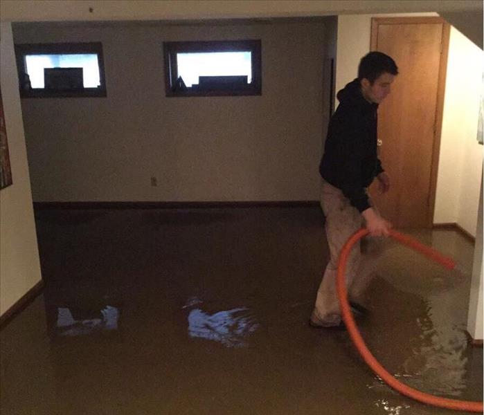 Flooded beige floor, technician with hose sucking up water.